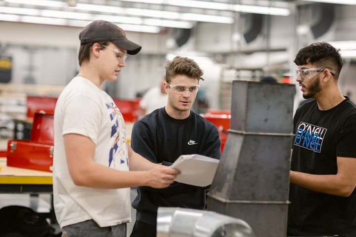 A group of students are standing in a Trades workshop wearing protective glasses.