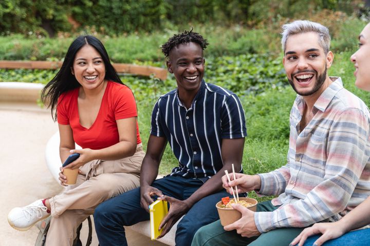 A group of students are sitting outside laughing and eating food.